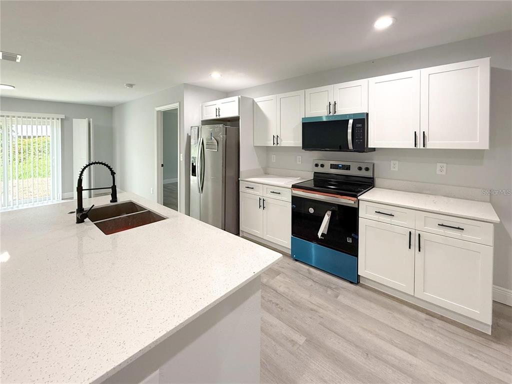 A modern kitchen features white cabinets, stainless steel appliances, and a large quartz-topped island — 608 COUGAR BOULEVARD, SEBRING, FL