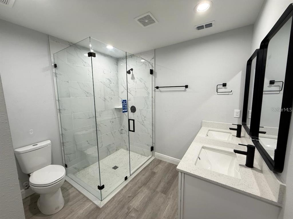 A modern bathroom features a glass-enclosed shower, double vanity, and a white toilet — 608 COUGAR BOULEVARD, SEBRING, FL