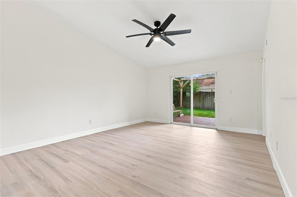 An empty room with light wood-look flooring, a black ceiling fan, and sliding glass doors — 723 OAK MANOR CIRCLE, ORLANDO, FL