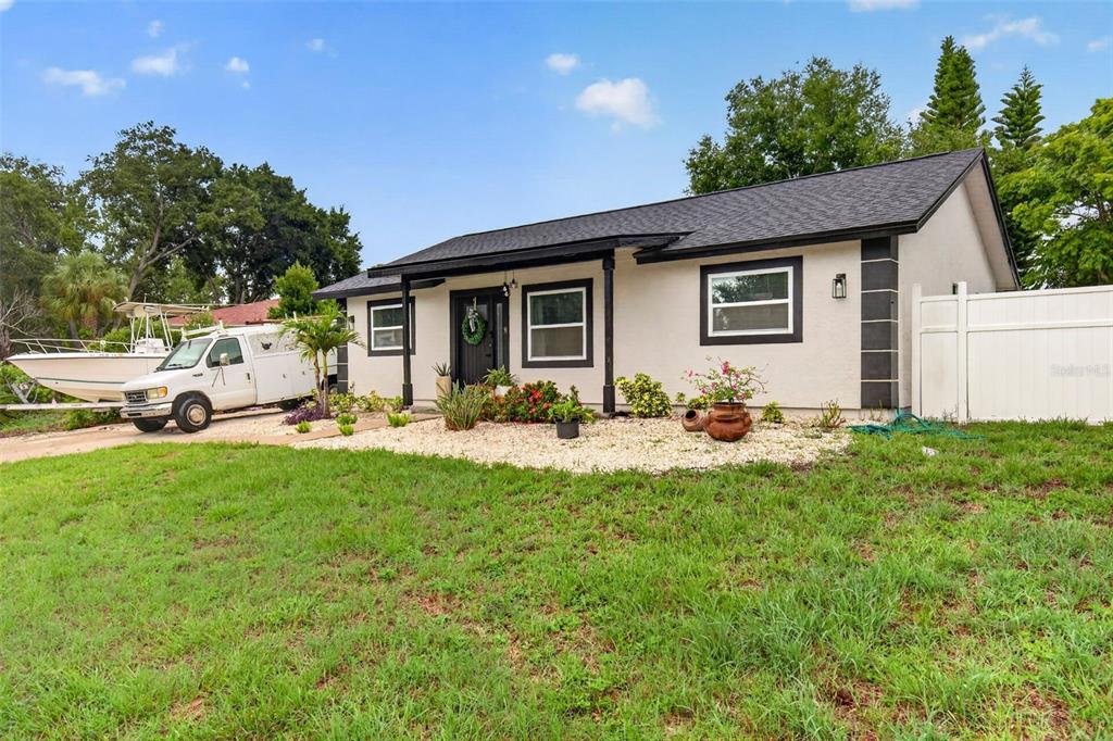 A single-story house with a white stucco exterior, dark trim, and a gravel front yard — 1435 BURNING TREE ROAD, TARPON SPRINGS, FL