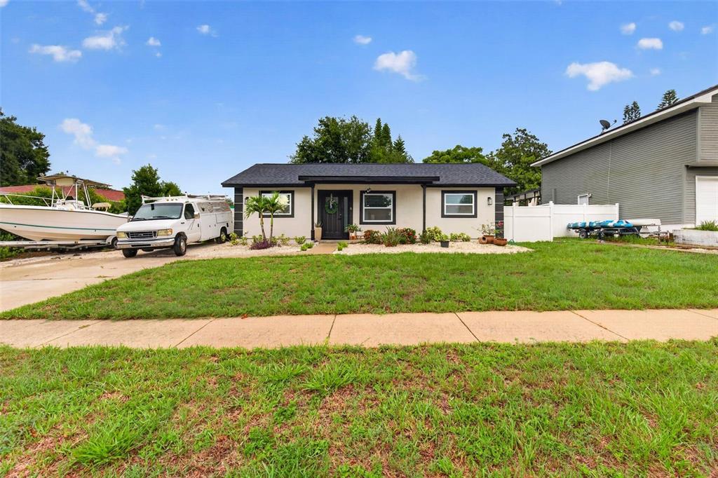 A single-story house with a white exterior, dark roof, and a front yard with grass — 1435 BURNING TREE ROAD, TARPON SPRINGS, FL