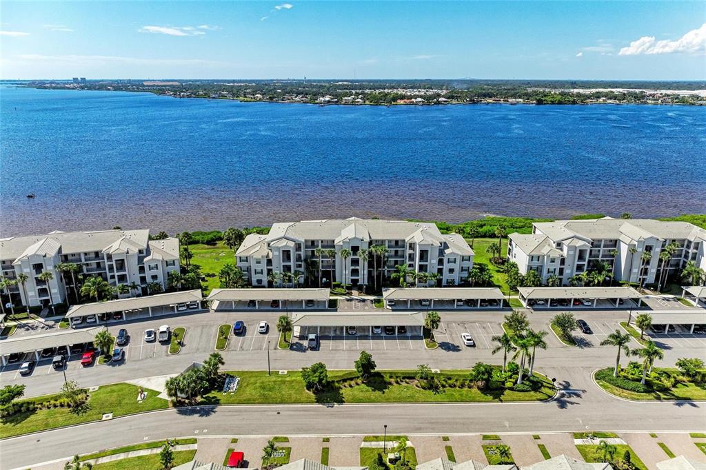 An aerial view shows three multi-story apartment buildings with covered parking lots near a bay — 1010 TIDEWATER SHORES LOOP UNIT 304, BRADENTON, FL