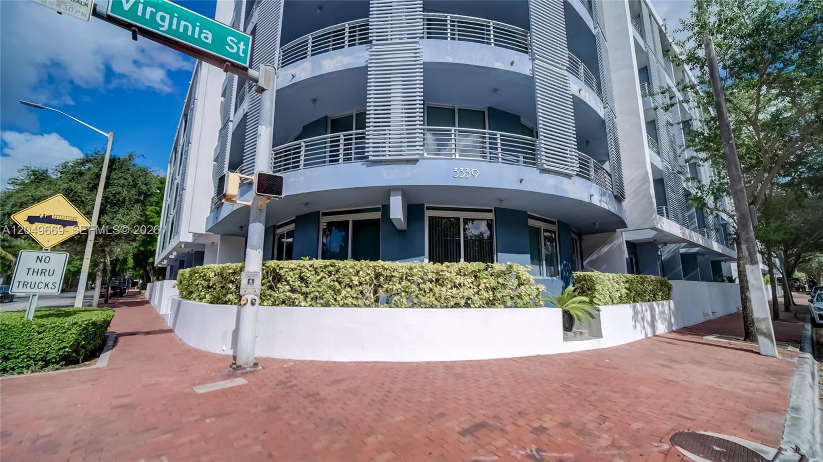 A multi-story blue apartment building with curved balconies stands on a corner with brick sidewalks — 3339 Virginia St # 323, Miami FL 33133, MIAMI, FL