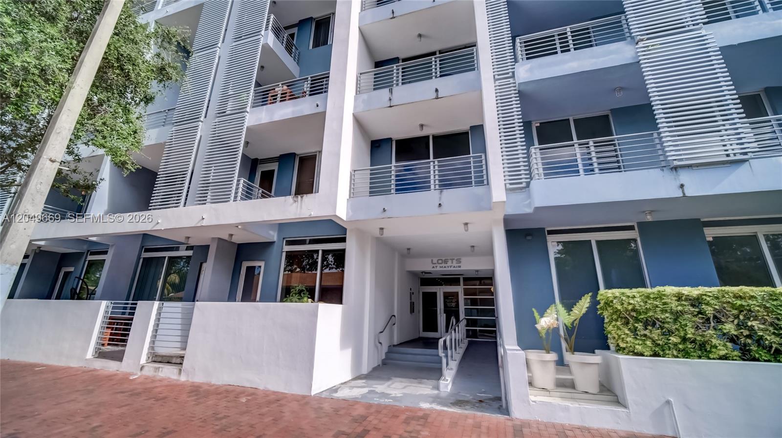 The exterior of a multi-story blue apartment building features balconies and a ground-level entrance — 3339 Virginia St # 323, Miami FL 33133, MIAMI, FL