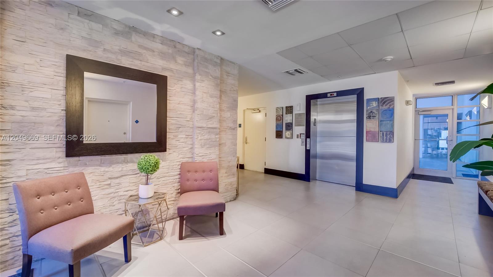 A modern building lobby features a stone accent wall, two pink chairs, and an elevator — 3339 Virginia St # 323, Miami FL 33133, MIAMI, FL