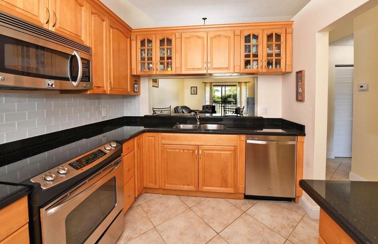 A kitchen with light wood cabinets, black countertops, stainless steel appliances, and a pass-through window — 22088 Palms Way # 204, Boca Raton FL 33433, BOCA RATON, FL