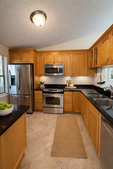 A kitchen features light wood cabinets, stainless steel appliances, black countertops, and tile flooring — 22088 Palms Way # 204, Boca Raton FL 33433, BOCA RATON, FL