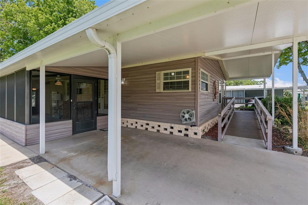 A covered carport with a concrete floor, a screened-in porch, and a wooden wheelchair ramp — 938 BLUE HERON BOULEVARD, OSTEEN, FL