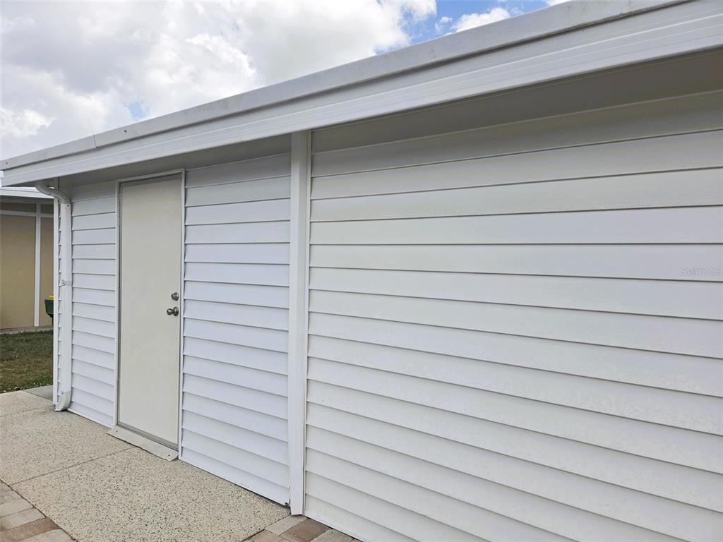 A white exterior wall with horizontal siding and a single door on a paved patio — 3221 SUMAC TERRACE, SARASOTA, FL
