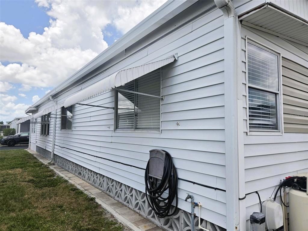 The exterior of a white mobile home features horizontal siding, metal window awnings, and lattice skirting — 3221 SUMAC TERRACE, SARASOTA, FL