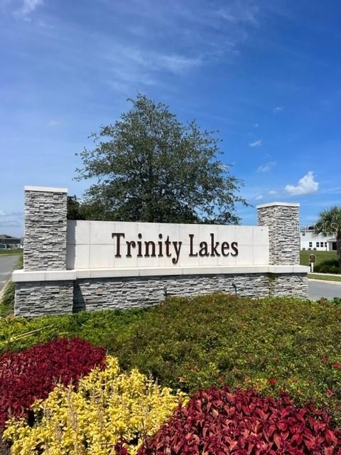 A stone monument sign for Trinity Lakes stands in front of a tree and sky — 7276 ROLLING LEAF ROAD, GROVELAND, FL