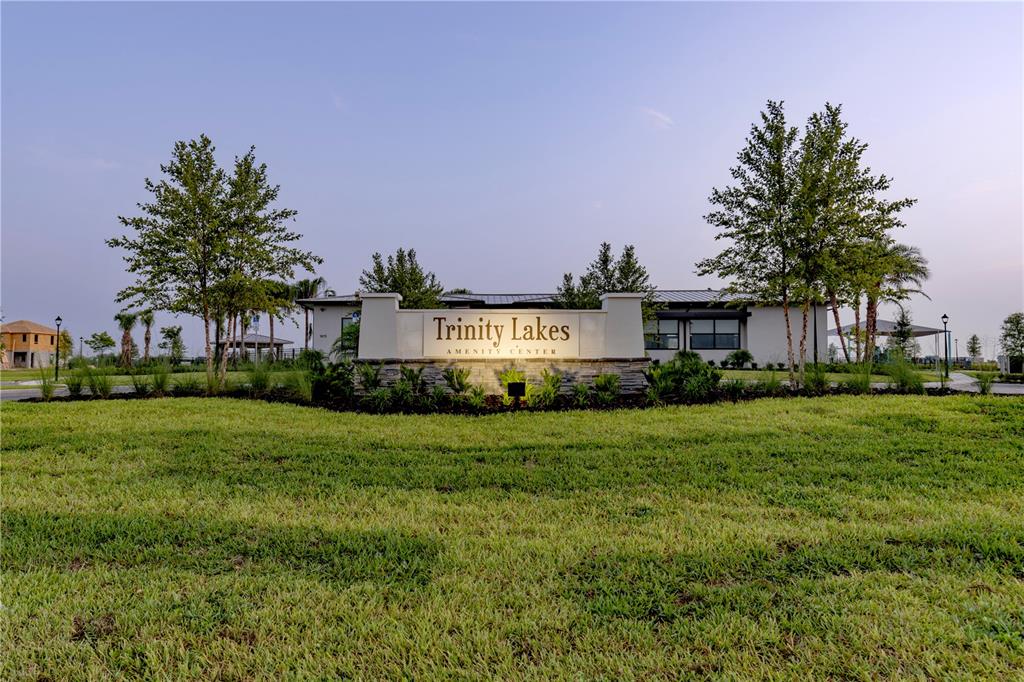 A stone monument sign for Trinity Lakes Amenity Center stands before a modern community building — 7276 ROLLING LEAF ROAD, GROVELAND, FL