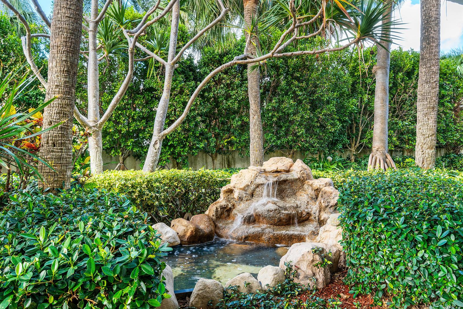 A small stone waterfall feature sits in a lush garden surrounded by trees and shrubs — 4600 S Ocean Boulevard # 602, Highland Beach FL 33487, HIGHLAND BEACH, FL