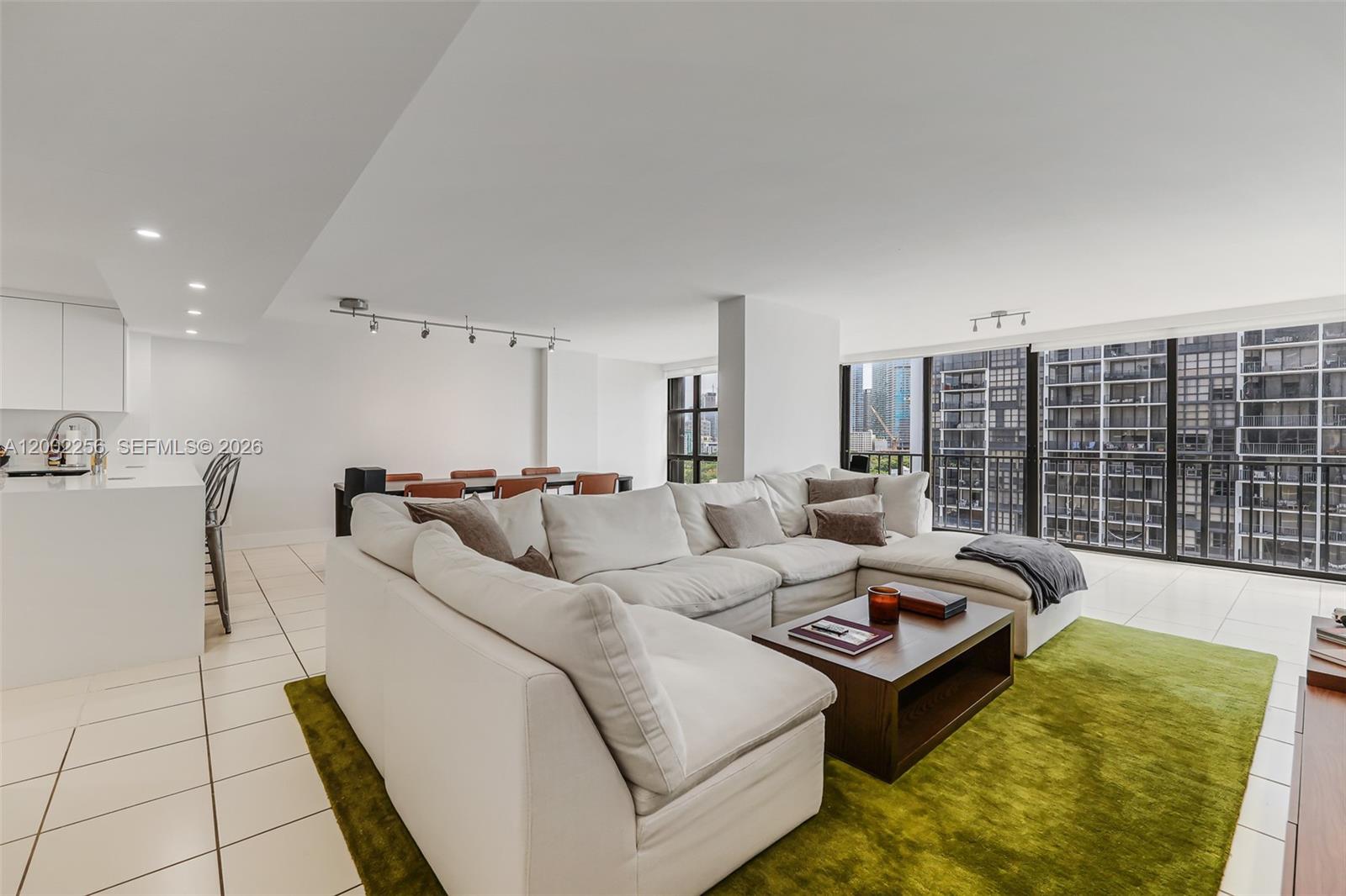 A modern living room features a white sectional sofa, green rug, and floor-to-ceiling windows — 1915 Brickell Ave # C1404, Miami FL 33129, MIAMI, FL