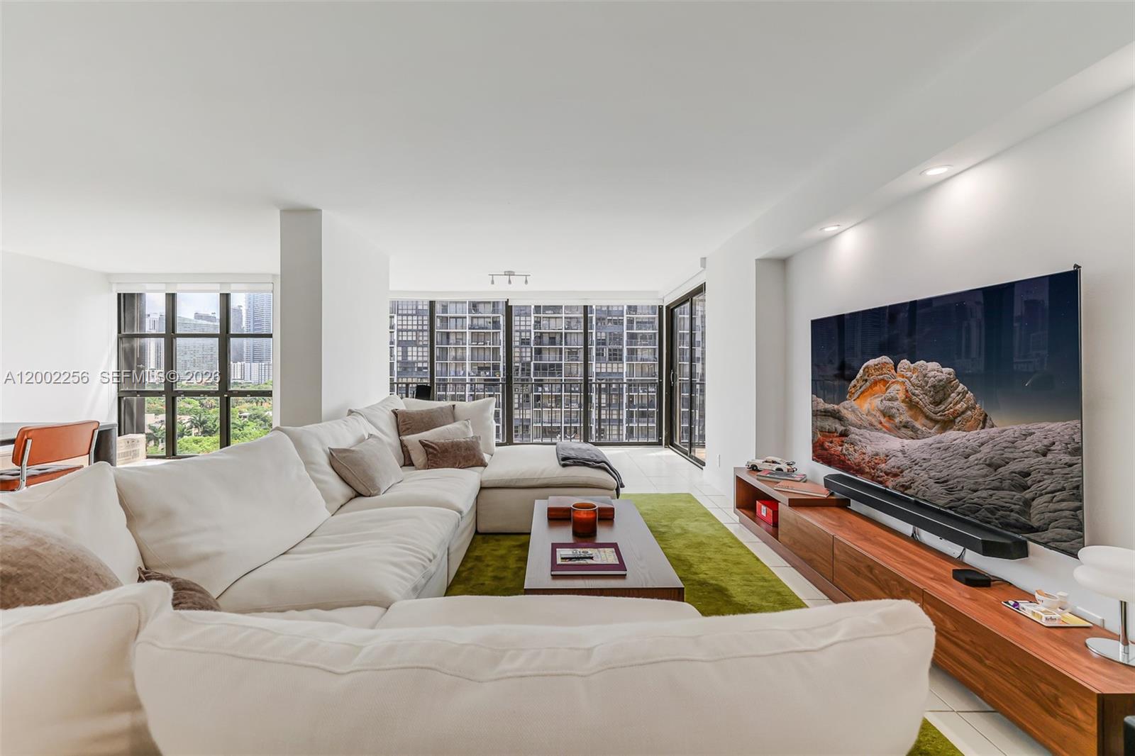 A modern living room features a large white sectional sofa, a green rug, and a television — 1915 Brickell Ave # C1404, Miami FL 33129, MIAMI, FL