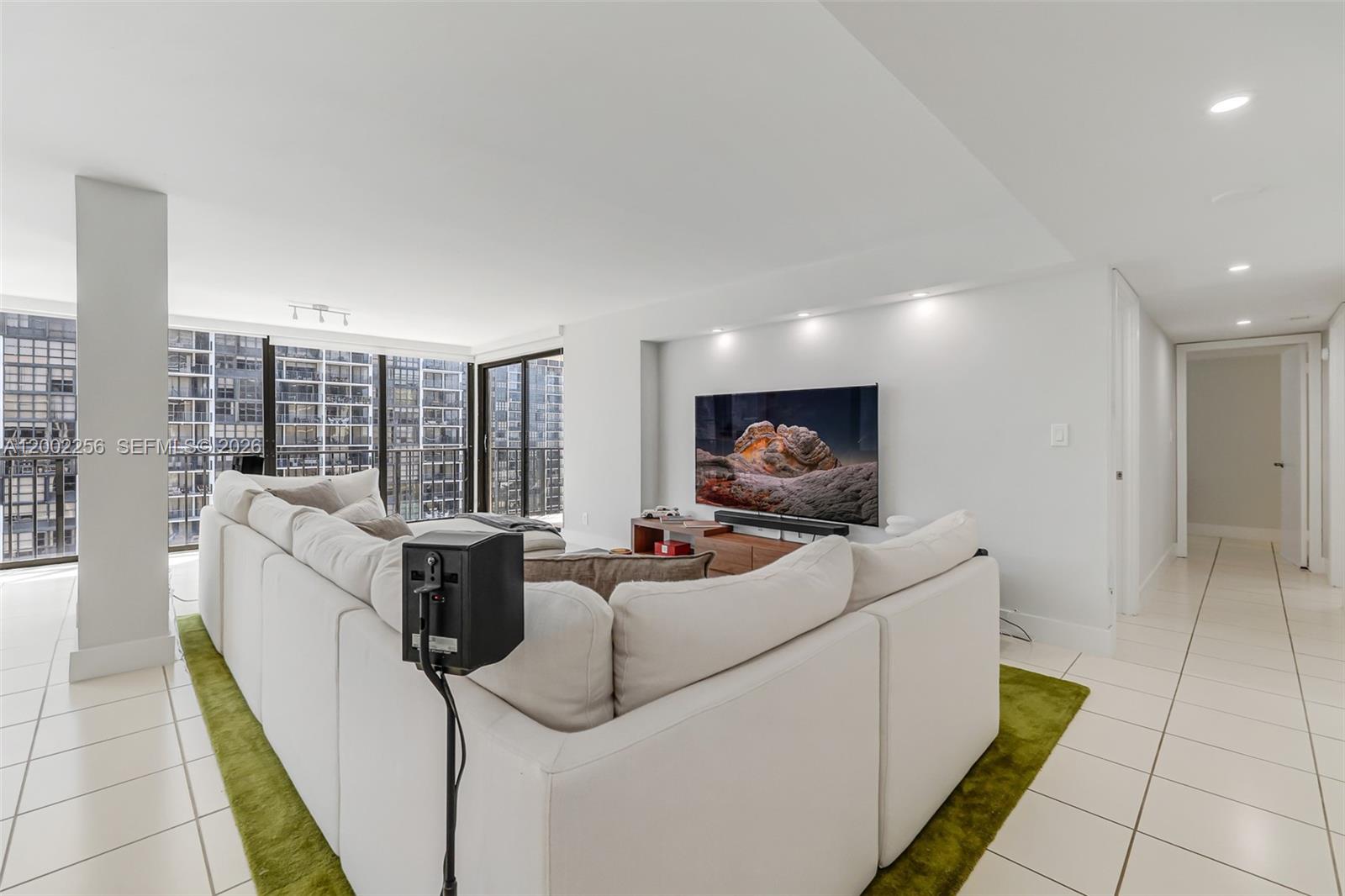 A living room features a white sectional sofa, a green rug, and a wall-mounted television — 1915 Brickell Ave # C1404, Miami FL 33129, MIAMI, FL