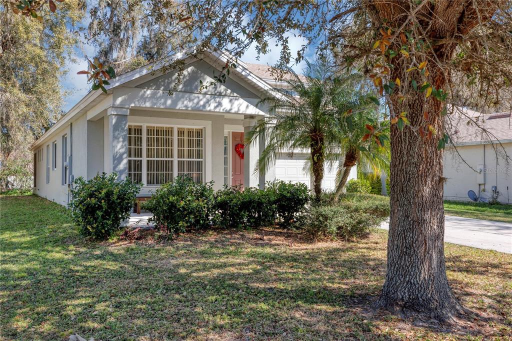 A single-story house with a covered porch, a red front door, and a large front tree — 2193 GRANGER AVENUE, KISSIMMEE, FL