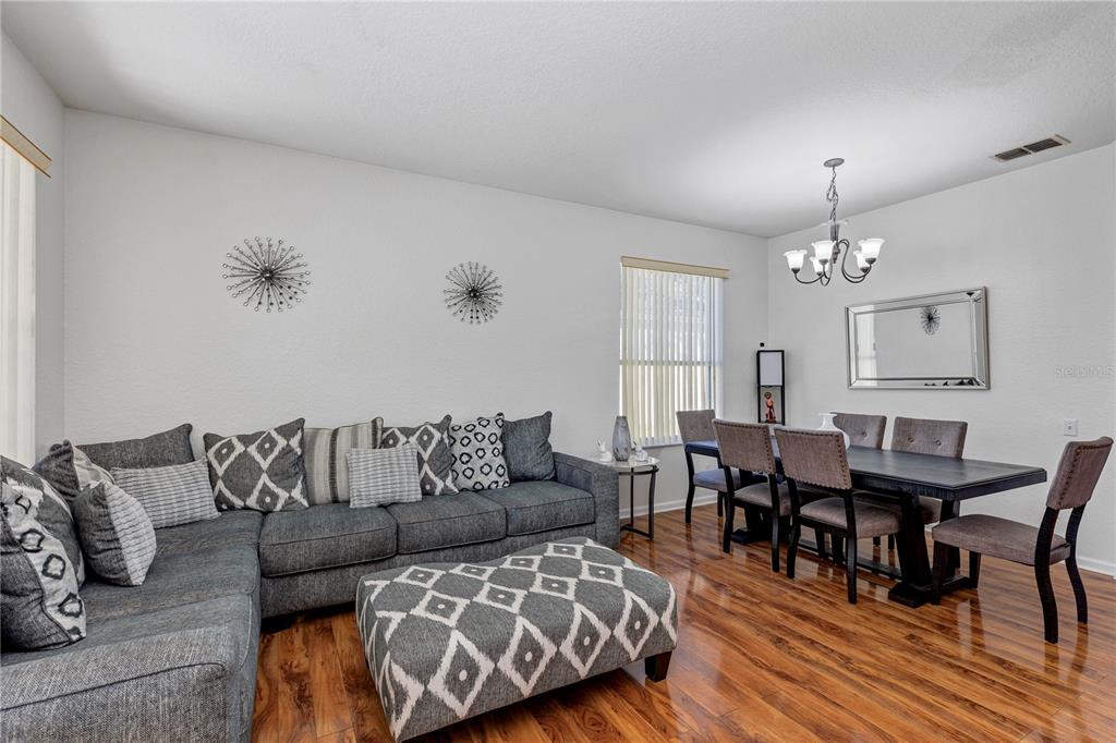 A living and dining area features a gray sectional sofa, patterned ottoman, and wooden flooring — 2193 GRANGER AVENUE, KISSIMMEE, FL