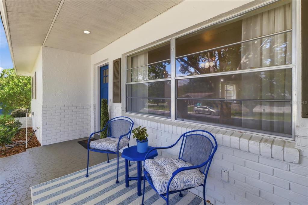 A covered porch features two blue metal chairs, a small table, and a white brick wall — 203 S LEE STREET, BEVERLY HILLS, FL