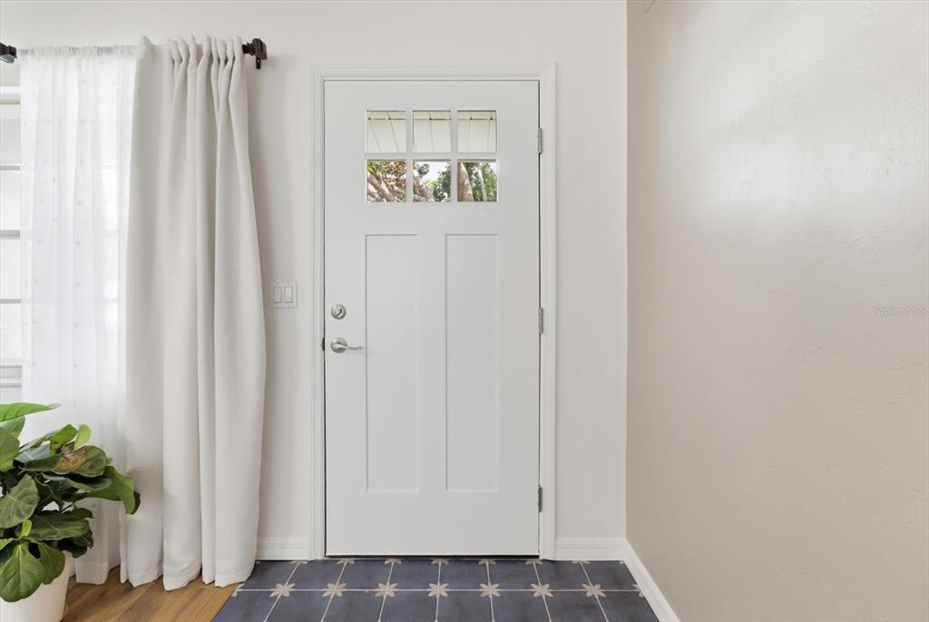 A white front door with a six-pane window sits beside a curtained window and tiled floor — 203 S LEE STREET, BEVERLY HILLS, FL