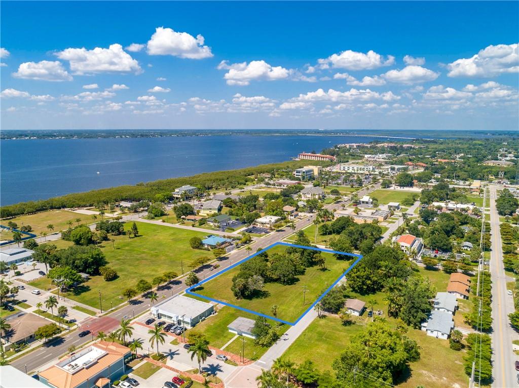 An aerial view shows a vacant, tree-covered rectangular lot outlined in blue near a waterfront — 427,407, 417, 425 E OLYMPIA AVENUE, PUNTA GORDA, FL