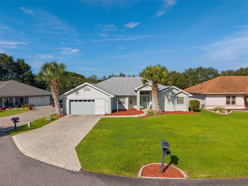 A single-story house with a light-colored exterior, a paved driveway, and two palm trees — 17566 SE 112TH AVENUE, SUMMERFIELD, FL
