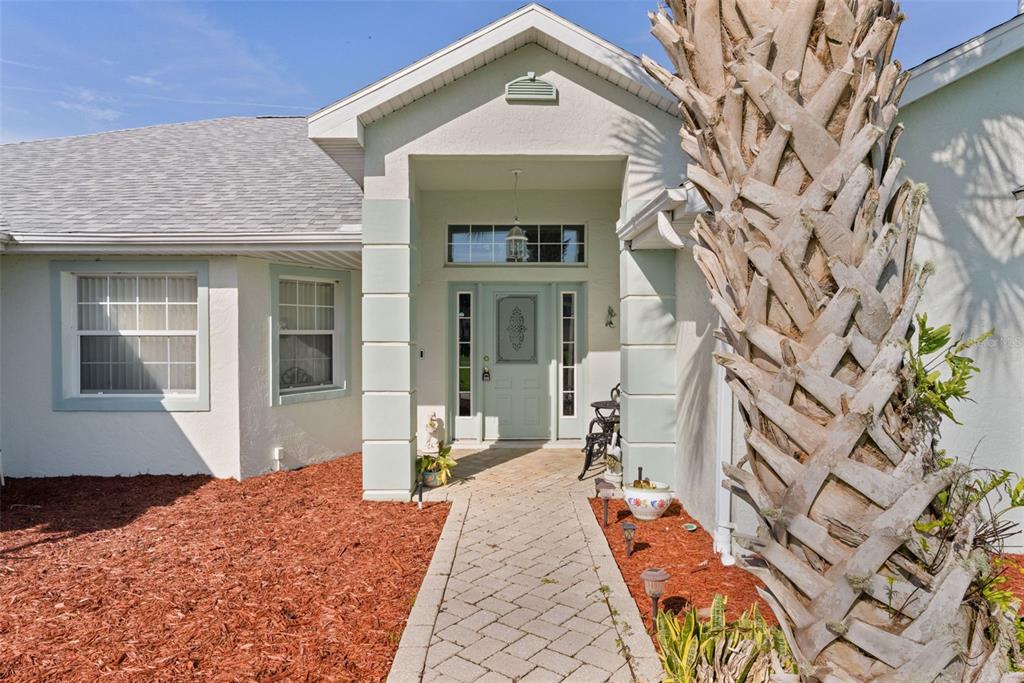 A paved walkway leads to the front entrance of a house with light green trim — 17566 SE 112TH AVENUE, SUMMERFIELD, FL