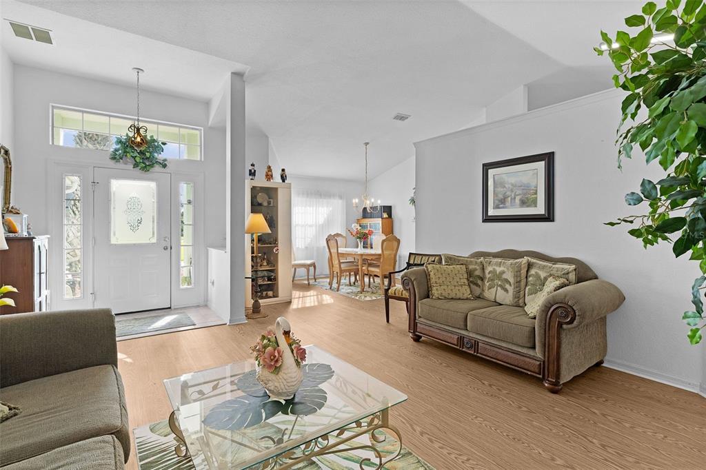 A living room with light wood flooring, a glass coffee table, and a dining area — 17566 SE 112TH AVENUE, SUMMERFIELD, FL