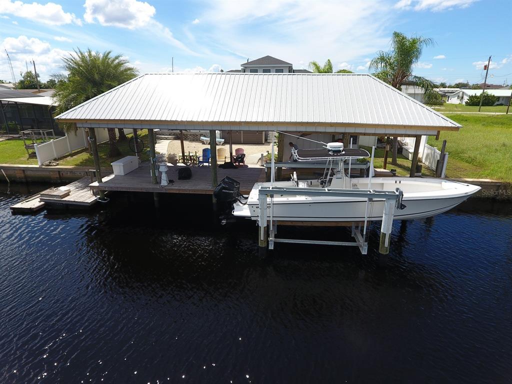 A white boat sits on a lift under a covered dock on a canal — 112 LELAND STREET SE, PORT CHARLOTTE, FL