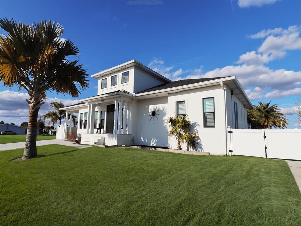 A white, two-story house with a palm tree in the front yard under a blue sky — 112 LELAND STREET SE, PORT CHARLOTTE, FL