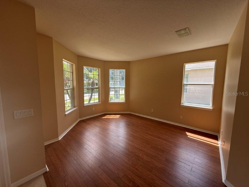 An empty room with tan walls, wood-look flooring, and a bay window — 1102 MAGNOLIA BLOSSOM COURT, APOPKA, FL