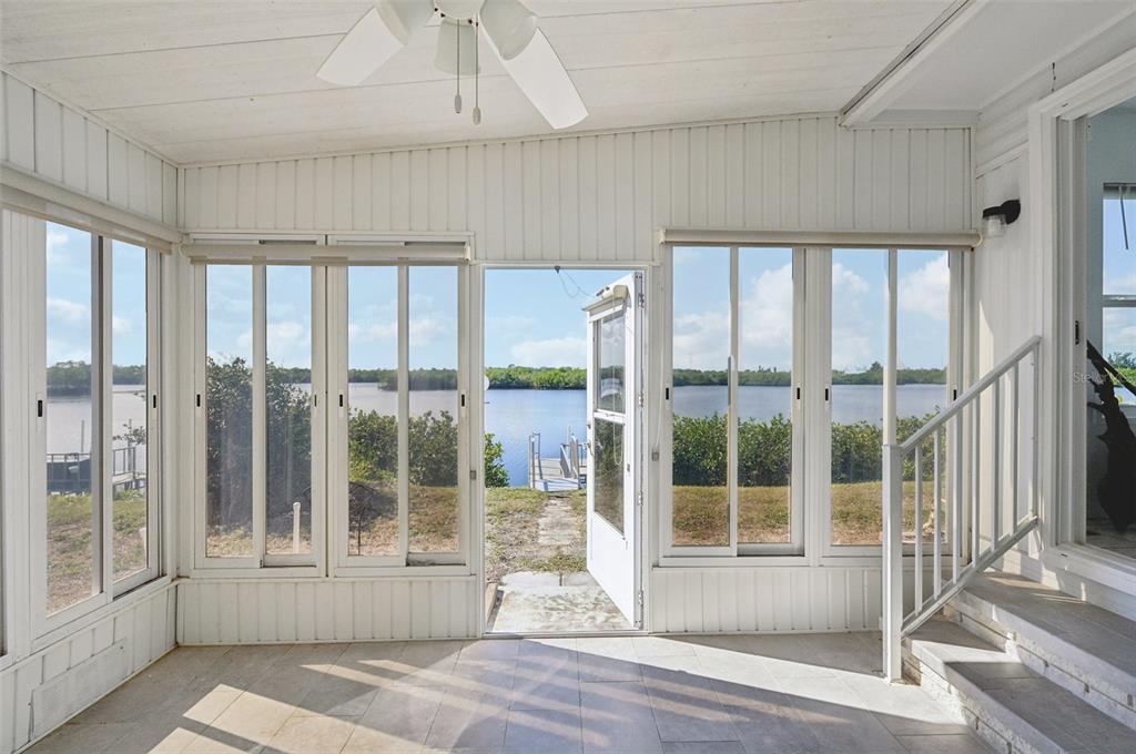 A sunroom with white walls, tile flooring, and large windows overlooking a lake and dock — 156 MARTINIQUE ROAD, NORTH PORT, FL