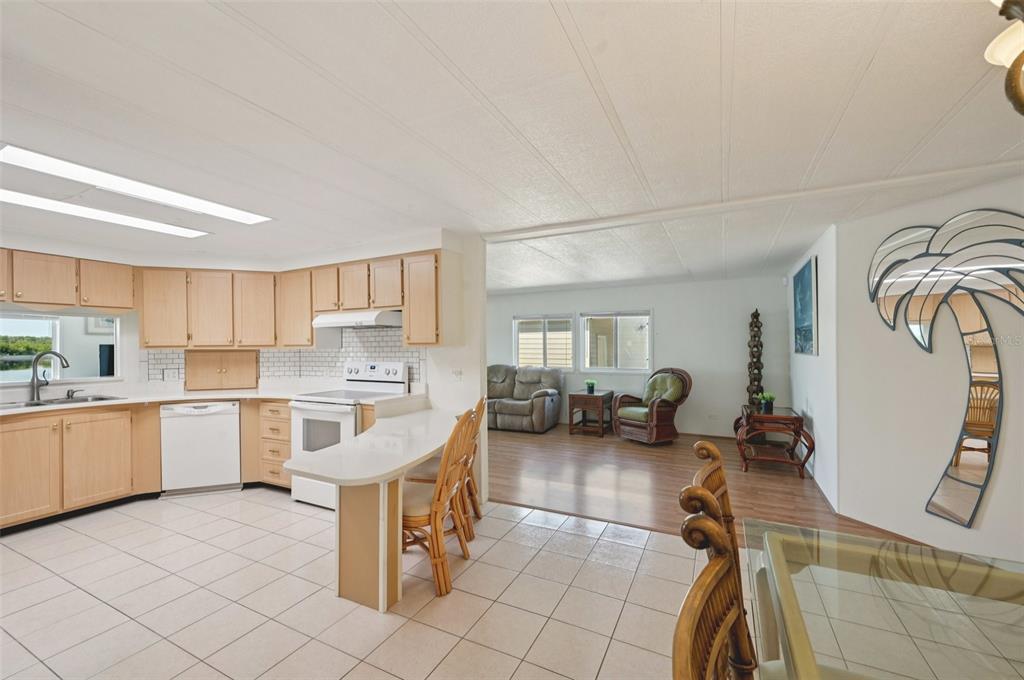 A kitchen with light wood cabinets and tile flooring opens into a living area — 156 MARTINIQUE ROAD, NORTH PORT, FL