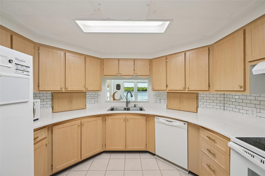 A kitchen features light wood cabinets, white countertops, a subway tile backsplash, and a sink — 156 MARTINIQUE ROAD, NORTH PORT, FL