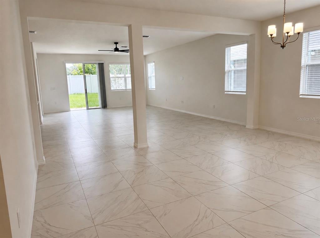 An open-concept living and dining area features white tile flooring and a sliding glass door — 1911 MAPLE PLUM COURT, SANFORD, FL