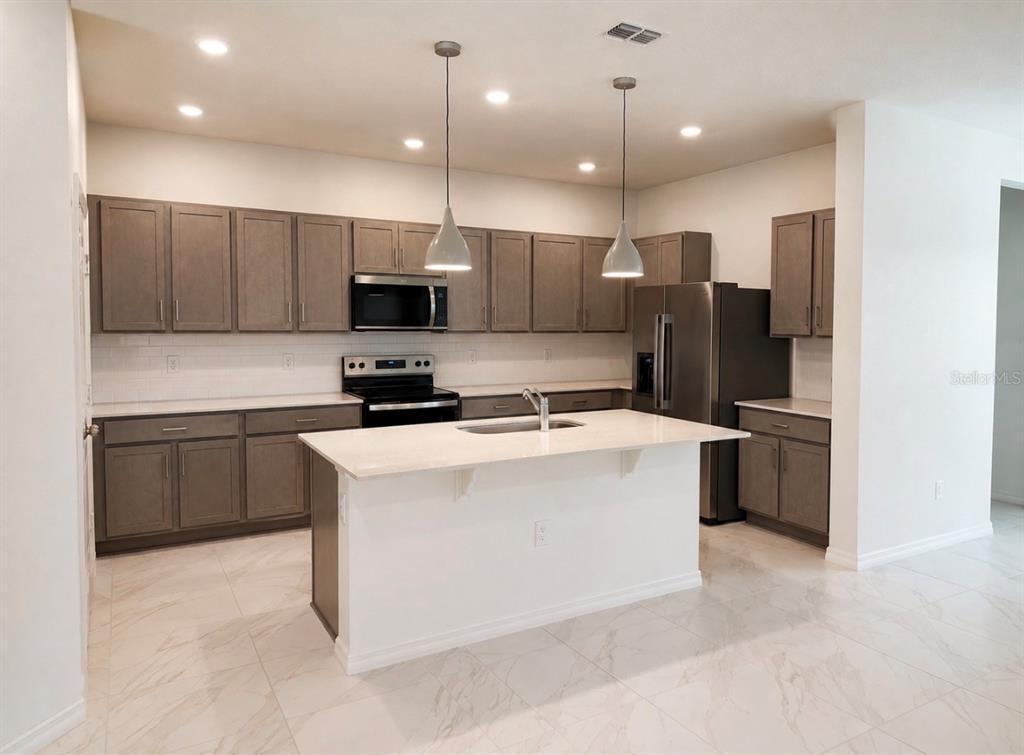 A modern kitchen features gray cabinets, white countertops, a central island, and stainless steel appliances — 1911 MAPLE PLUM COURT, SANFORD, FL
