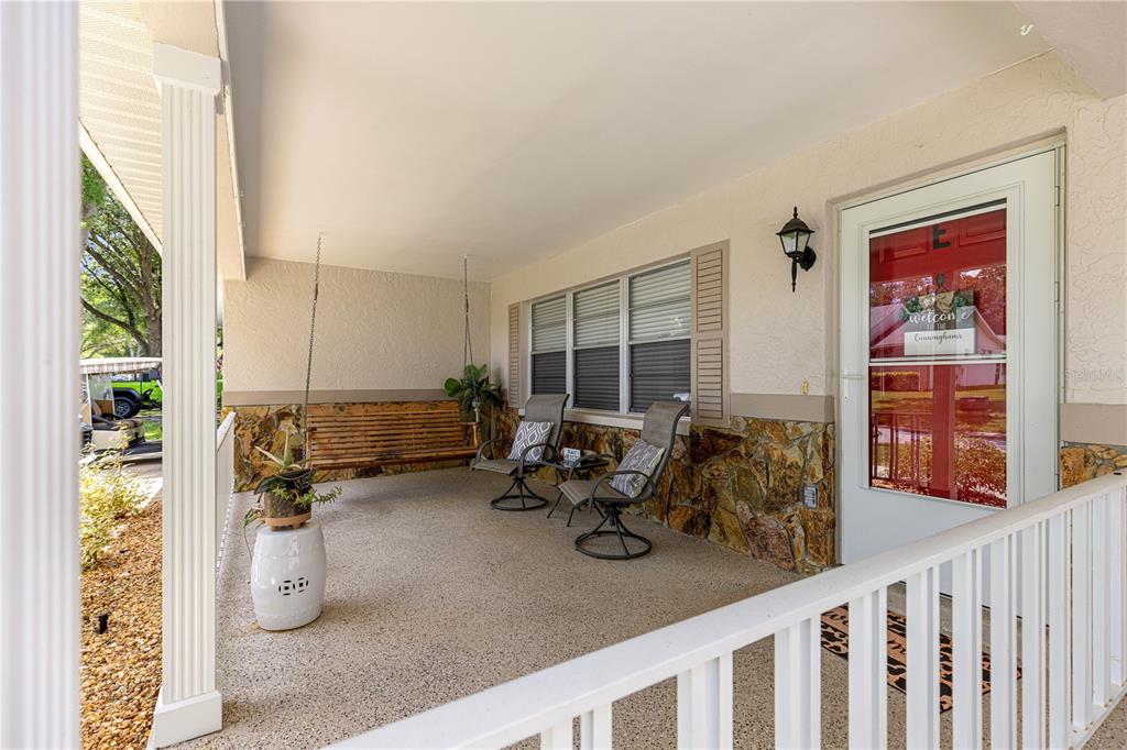 A covered front porch features a hanging wooden bench, two chairs, and stone siding — 8874 SW 95TH STREET UNIT E, OCALA, FL