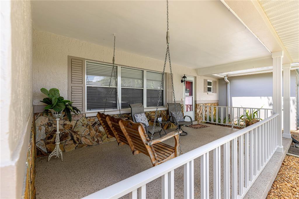 A covered front porch features a wooden swing, stone siding, and a white railing — 8874 SW 95TH STREET UNIT E, OCALA, FL