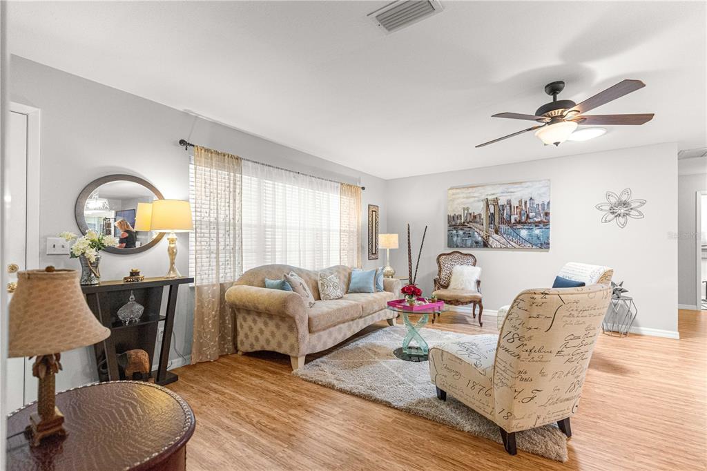 A living room features light wood flooring, a beige sofa, and a patterned accent chair — 8874 SW 95TH STREET UNIT E, OCALA, FL