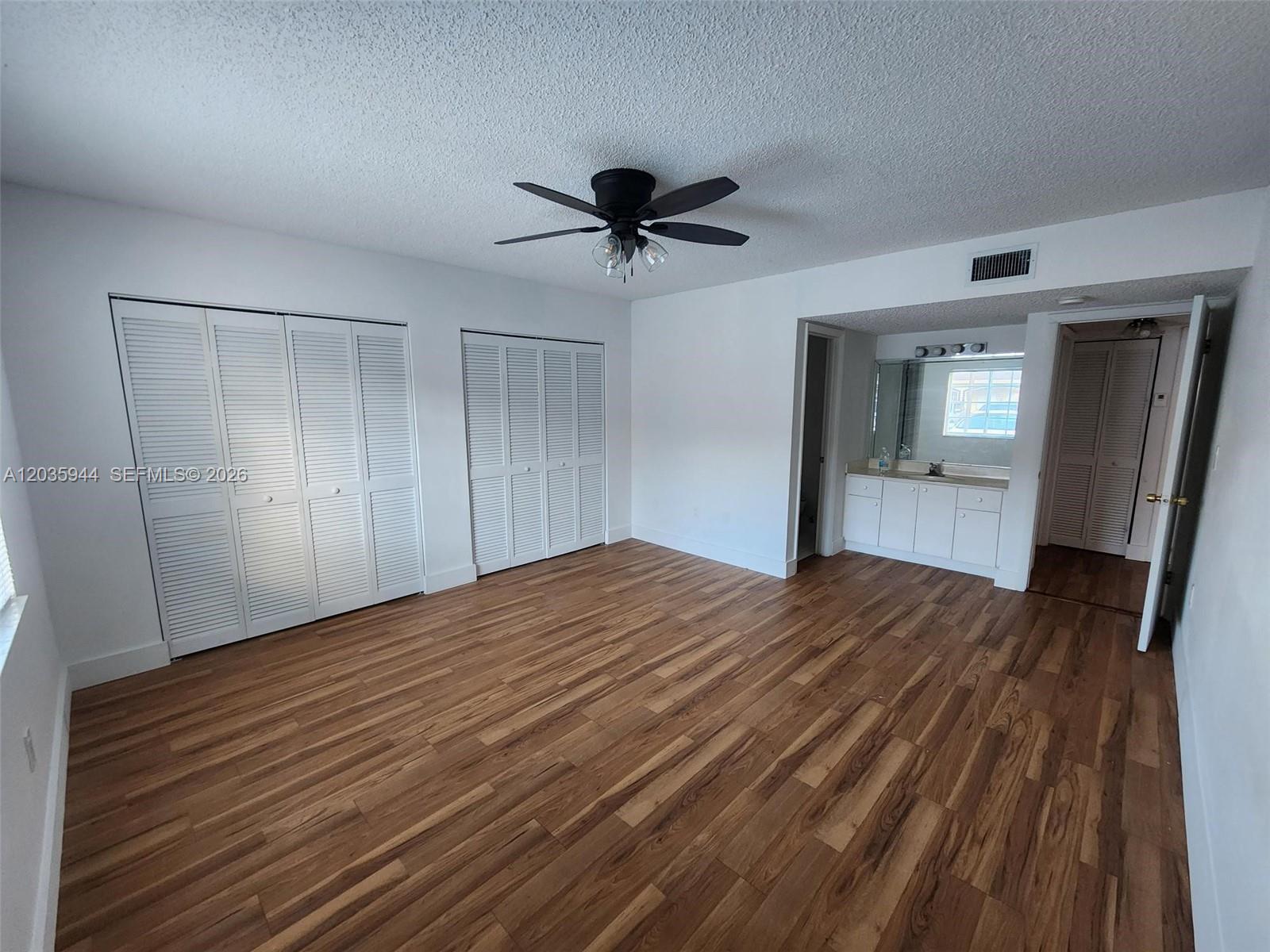 A bedroom features wood-look flooring, white louvered closet doors, a ceiling fan, and an attached vanity — 10019 W Okeechobee Rd # 102, Hialeah Gardens FL 33016, HIALEAH GARDENS, FL
