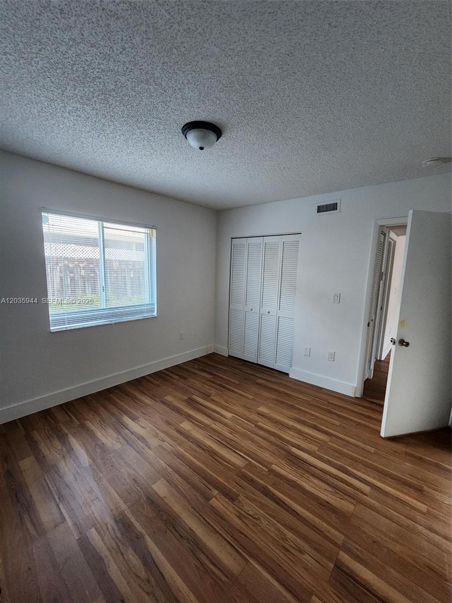 An empty bedroom features wood-look flooring, white walls, a window with blinds, and a closet — 10019 W Okeechobee Rd # 102, Hialeah Gardens FL 33016, HIALEAH GARDENS, FL