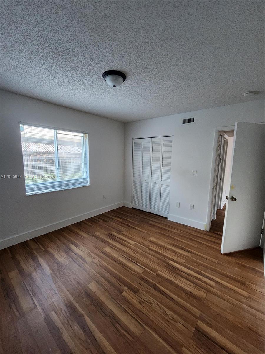 An empty bedroom features wood-look flooring, white walls, a window, and a white closet — 10019 W Okeechobee Rd # 102, Hialeah Gardens FL 33016, HIALEAH GARDENS, FL