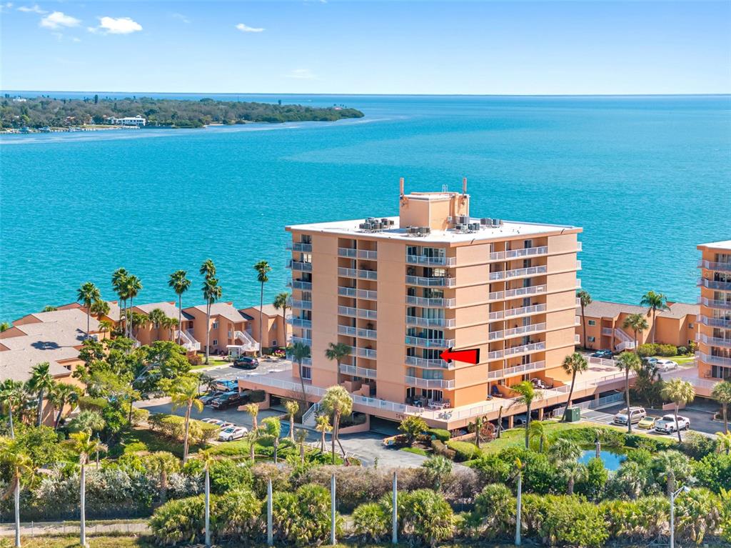 An aerial view shows a multi-story peach-colored apartment building situated along a waterfront — 7430 SUNSHINE SKYWAY LANE S UNIT 406, ST PETERSBURG, FL