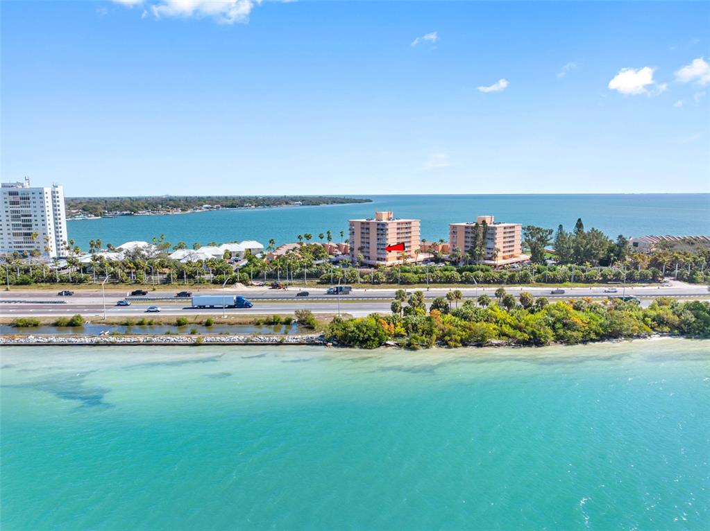 An aerial view shows a coastal highway running between a turquoise bay and residential buildings — 7430 SUNSHINE SKYWAY LANE S UNIT 406, ST PETERSBURG, FL