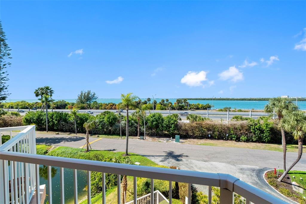 A balcony overlooks a road, palm trees, and a body of water under a blue sky — 7430 SUNSHINE SKYWAY LANE S UNIT 406, ST PETERSBURG, FL