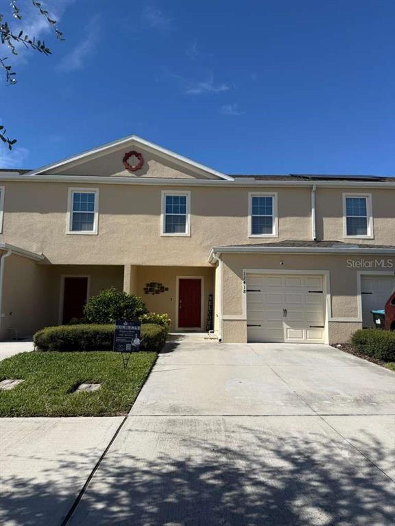 A two-story townhouse with a beige stucco exterior, a single-car garage, and a front lawn — 12418 BOWES BRANCH ROAD, ORLANDO, FL