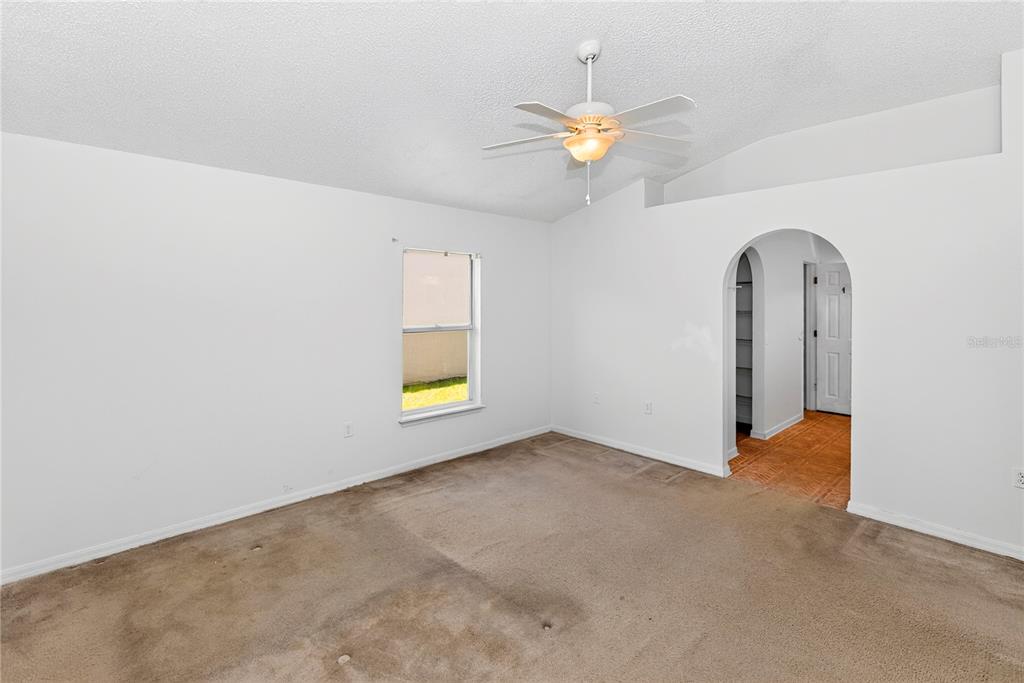 An empty bedroom features beige carpeting, white walls, a ceiling fan, and an arched doorway — 249 CURTIS AVENUE, GROVELAND, FL