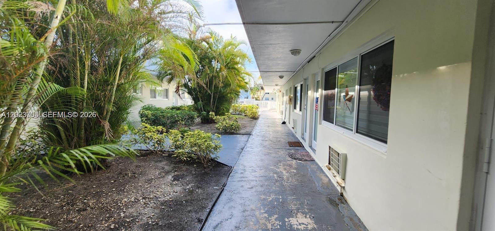 A paved walkway runs alongside a building exterior with windows and a window air conditioner — 1233 Marseille Dr # 5, Miami Beach FL 33141, MIAMI BEACH, FL