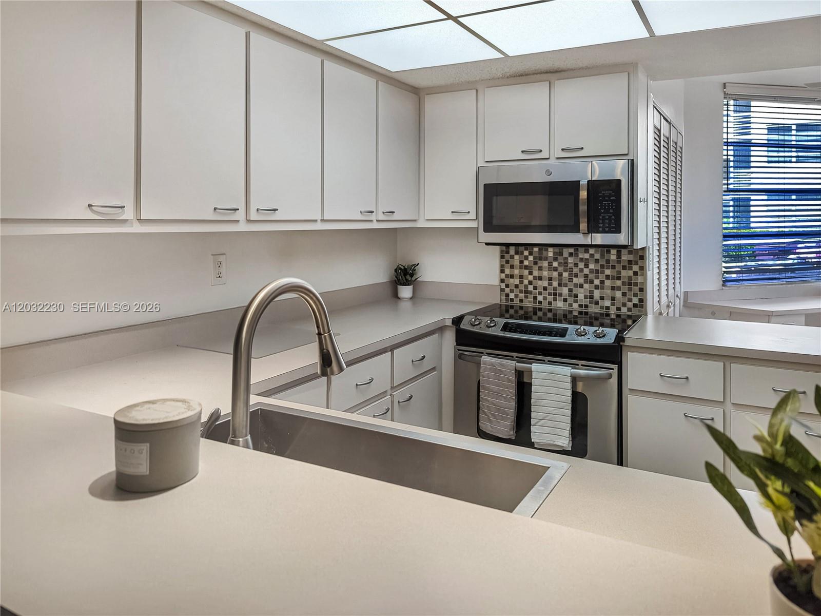 A kitchen features white cabinets, stainless steel appliances, a tiled backsplash, and a sink — 9531 Seagrape Dr # 108, Davie FL 33324, DAVIE, FL