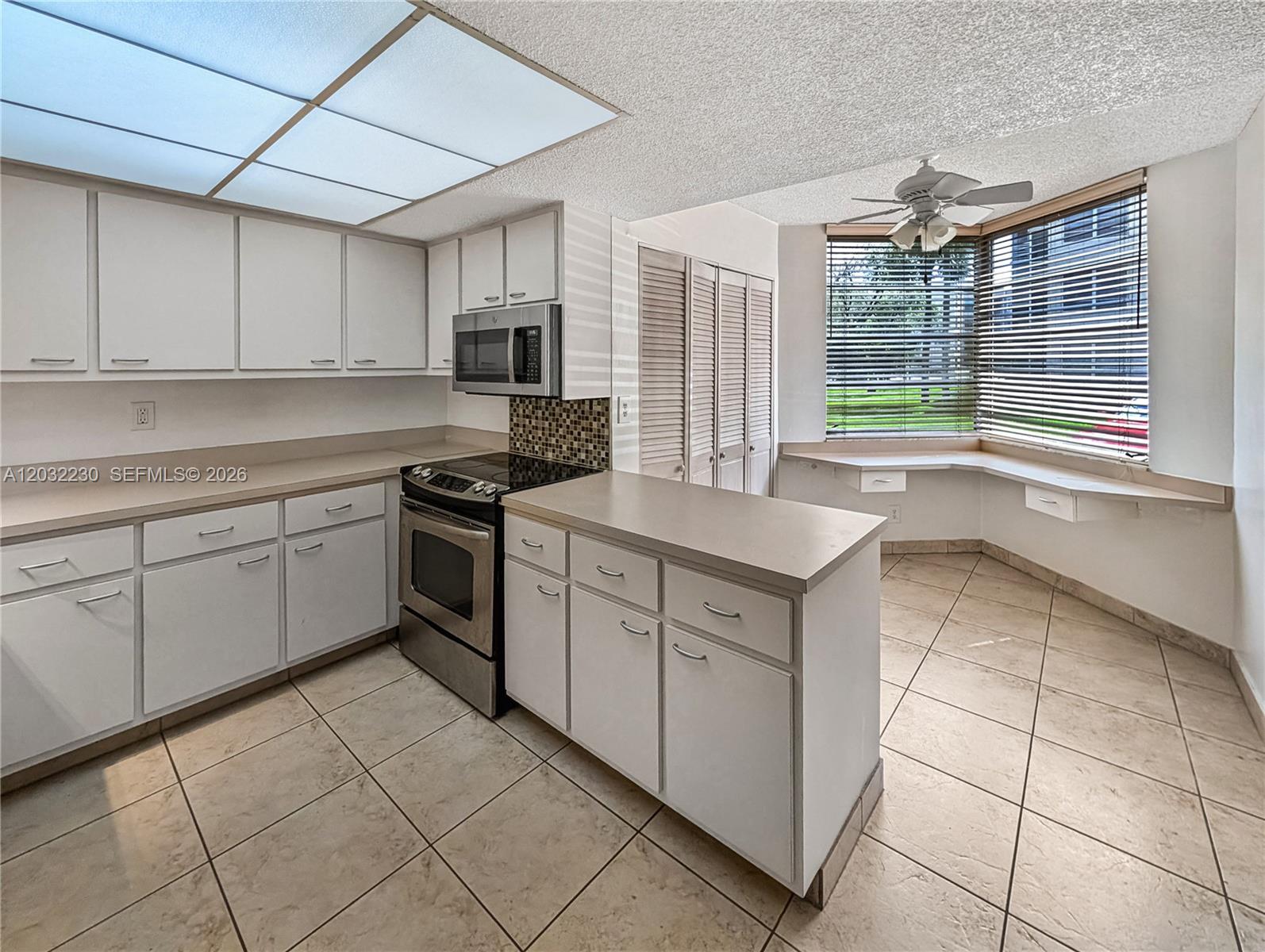 A kitchen features white cabinets, stainless steel appliances, tile flooring, and a windowed breakfast nook — 9531 Seagrape Dr # 108, Davie FL 33324, DAVIE, FL